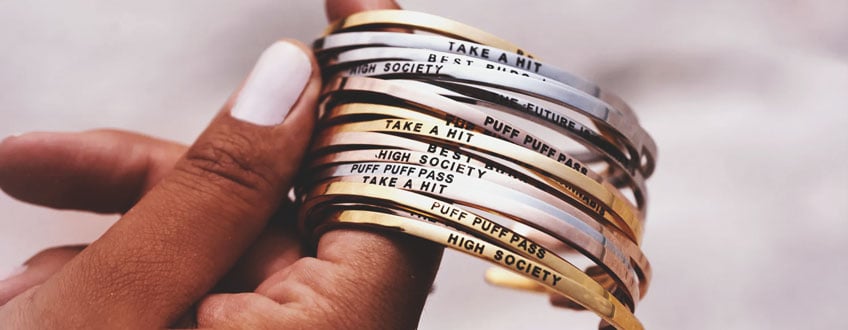 Une main tenant une pile de bracelets en or et argent avec différentes phrases gravées.