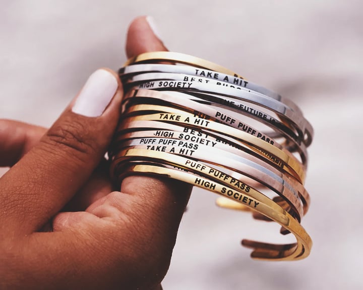 Une main tenant une pile de bracelets en or et argent avec différentes phrases gravées.