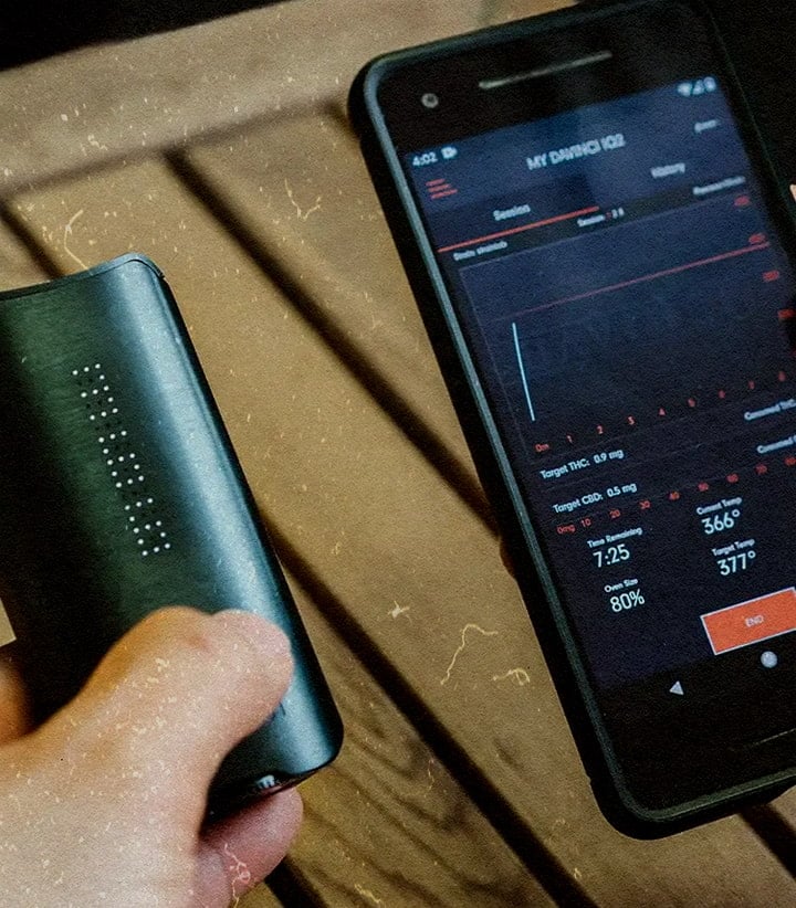 Vaporisateur DaVinci IQ3 : Fonctions de nouvelle génération et performance supérieure Vaporisateur PAX IQ3 avec appli montrant 80 % de batterie, THC 0,5 mg et 366 °F, tenu à côté d’un téléphone sur une table en bois.