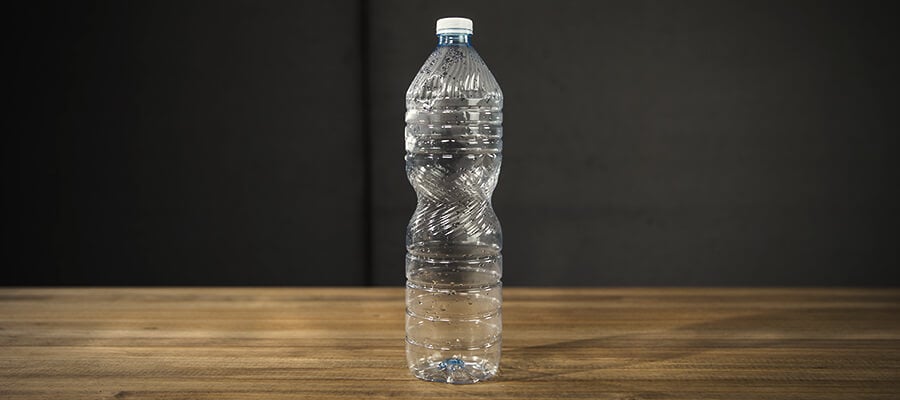Bouteille d'eau transparente avec un bouchon bleu, posée sur une surface en bois.