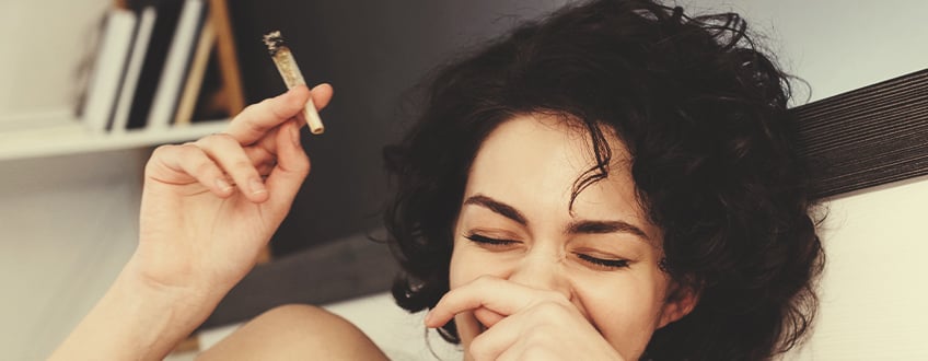 Personne riant en tenant un joint de cannabis.