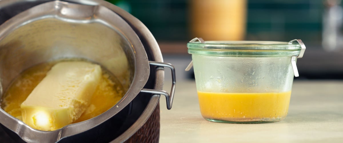 Du cannabutter fondu en cours de préparation dans une casserole, puis transféré dans un récipient en verre sur un plan de travail de cuisine.
