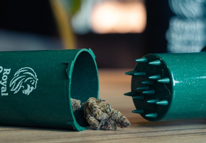 Grindtainer pour ranger et grinder facilement le cannabis Image d’un grindtainer compact avec des têtes de cannabis sur une surface en bois.