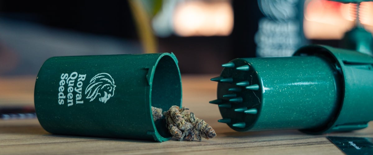 Grindtainer pour ranger et grinder facilement le cannabis Image d’un grindtainer compact avec des têtes de cannabis sur une surface en bois.