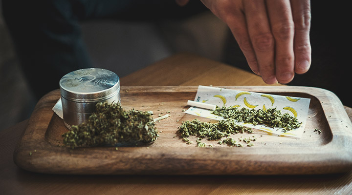 Personne remplissant un papier à rouler avec du cannabis moulu en utilisant le doigt.