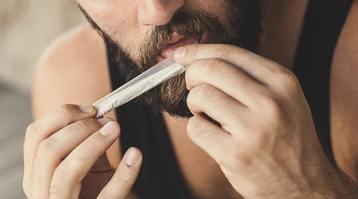 Personne scellant un joint de marijuana avec soin, en utilisant ses doigts pour s'assurer qu'il soit bien fermé, dans un environnement lumineux et détendu.