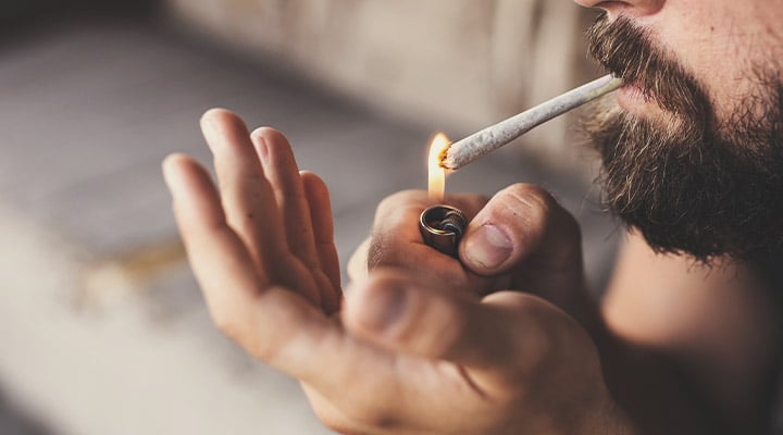 Personne allumant un joint avec un briquet, le tenant entre les lèvres.