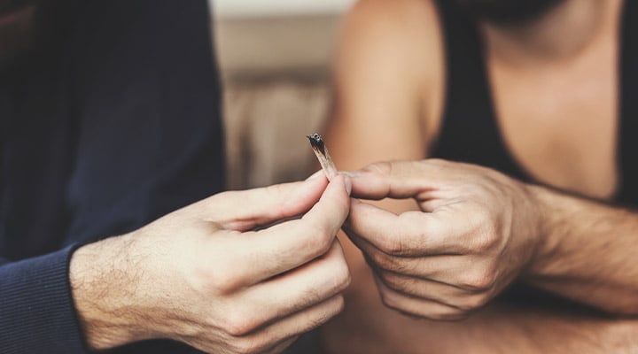 Deux personnes s'échangeant un joint dans un environnement détendu, avec un focus sur les mains et le geste de passer le joint.
