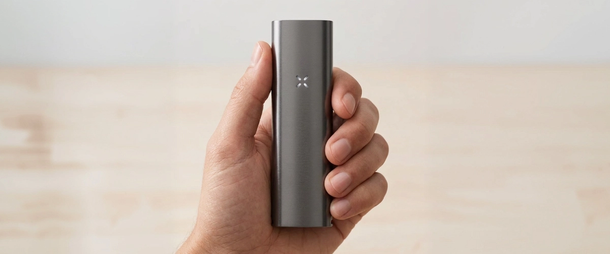 Vue produit du vaporisateur PAX Four tenu en main Vaporisateur PAX Four tenu dans une main, montrant son corps fin et mat, son format compact et son indicateur LED en pétales à l’avant