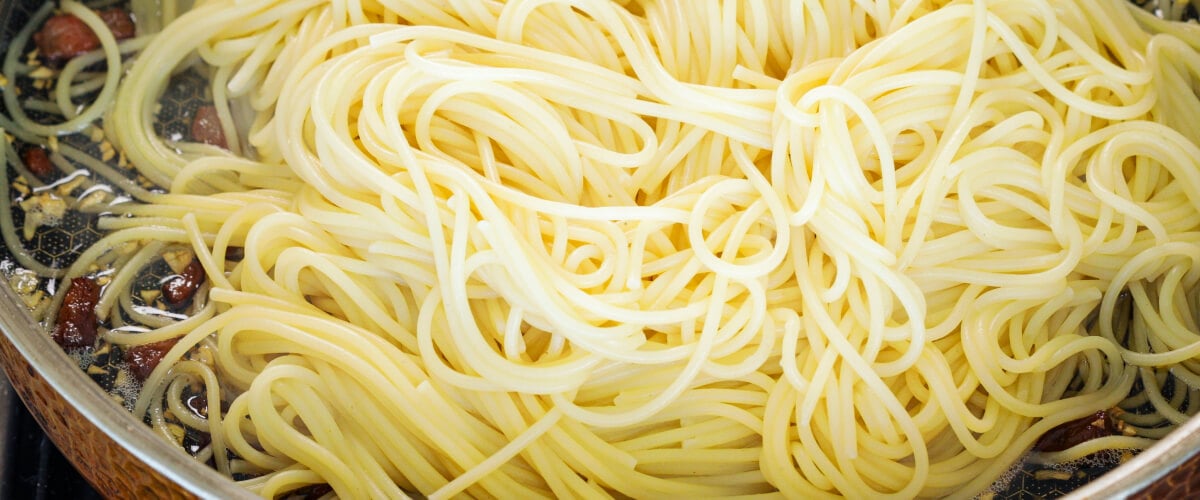 Spaghetti égouttés mélangés avec de la pancetta croustillante et du beurre infusé dans une poêle, quatrième étape pour une carbonara au cannabis