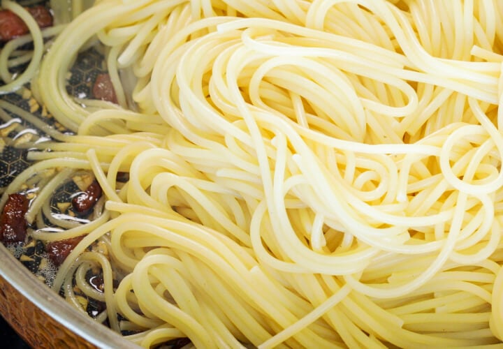 Spaghetti égouttés mélangés avec de la pancetta croustillante et du beurre infusé dans une poêle, quatrième étape pour une carbonara au cannabis
