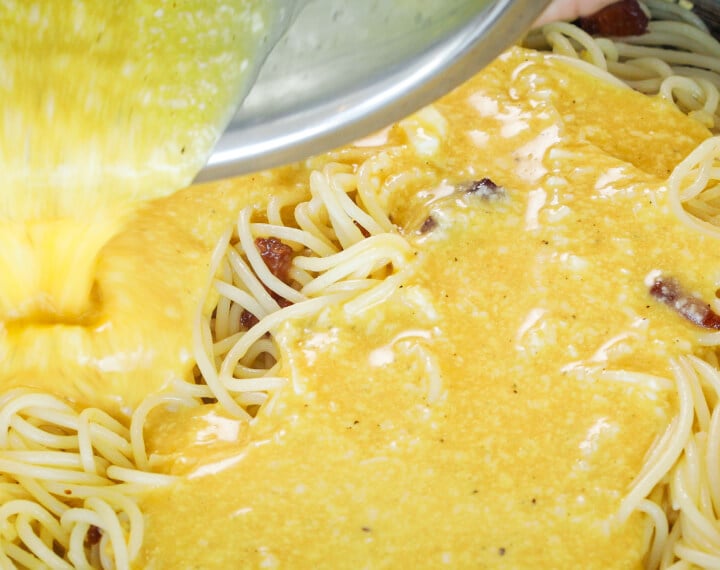 Mélange d’œufs et de fromage versé sur des spaghetti chauds dans une poêle, cinquième étape pour une carbonara infusée au cannabis